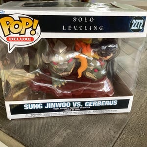May include: A Funko Pop Deluxe vinyl figure set featuring Sung Jinwoo vs. Cerberus from Solo Leveling. The figures are in a clear plastic display case. The box has the Funko Pop logo and the number 2272.