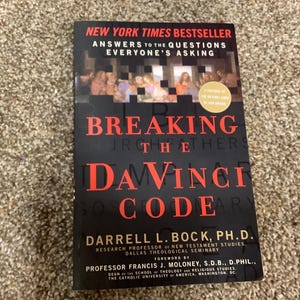 May include: A paperback book titled Breaking the Da Vinci Code by Darrell L. Bock, Ph.D. The black cover features red text, a New York Times Bestseller label, and a circular graphic. The subtitle reads Answers to the Questions Everyone's Asking.
