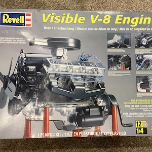 May include: A Revell Visible V-8 Engine plastic model kit box featuring a detailed image of a transparent engine with blue wires, a black fan, and orange supports. The box text indicates it is over 12 inches long and for experienced builders.