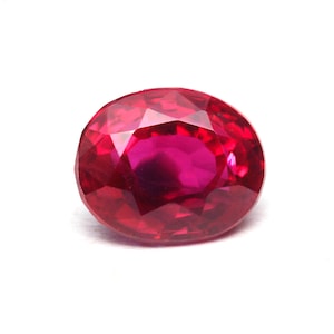 May include: A vibrant, oval-cut gemstone with a deep, saturated red color. The stone features a faceted surface that reflects light, creating a brilliant, sparkling appearance across its polished, translucent, and multi-faceted top surface.