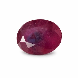 May include: A faceted, oval-shaped ruby gemstone. The gem is a deep red color with a hint of purple and displays internal inclusions. The cut of the stone creates multiple reflective surfaces, enhancing its brilliance. The ruby is set against a white background.