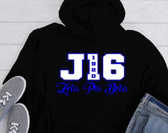 Puede incluir: Sudadera con capucha negra con texto blanco y azul. El texto dice "J16" con "1920" en el medio y "Zeta Phi Beta" debajo. La sudadera se combina con zapatillas grises y vaqueros azules.