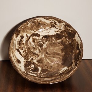 May include: A brown and white ceramic bowl with a marbled design. The bowl is round and has a slightly raised rim.