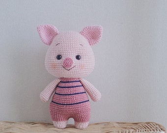 Può includere: Un giocattolo di amigurumi a forma di maiale rosa lavorato a uncinetto con abiti a righe blu e rosa. Il giocattolo è seduto su un cesto di vimini.