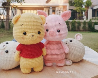 May include: A set of four crocheted stuffed animals: Winnie the Pooh, Piglet, Eeyore, and a mouse. The animals are all standing on a wooden surface. The background is a blurry image of a house and trees.