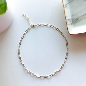 May include: A silver chain necklace with a delicate, linked chain design. The necklace is made of small, oval-shaped links.