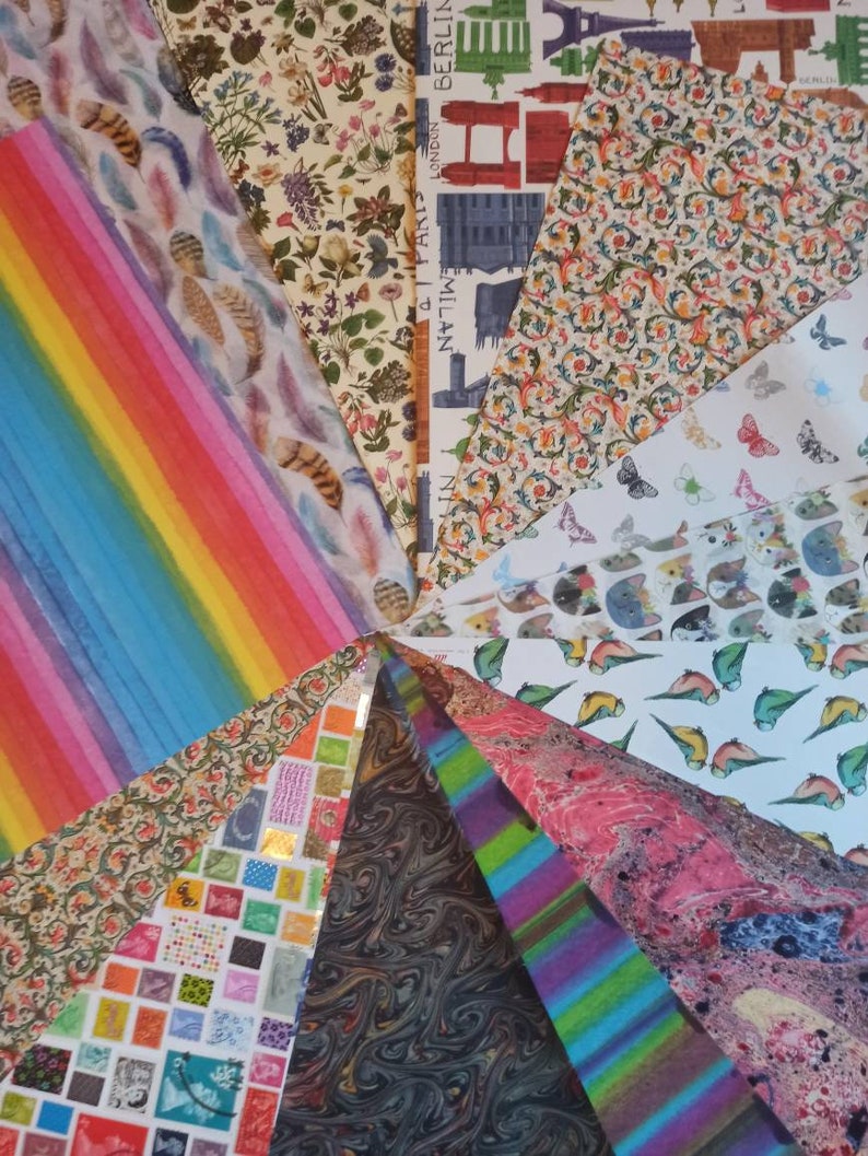 May include: A collection of colorful patterned wrapping paper featuring various designs, including feathers, stripes, butterflies, and city skylines. The papers are arranged in a fan shape, with the tips of each paper meeting in the center.