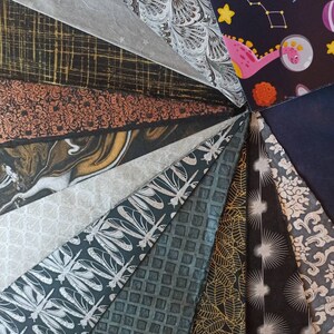 May include: A collection of 15 different patterned tissue papers in various colors, including black, white, gold, and silver. The papers are arranged in a fan shape, with the patterns visible on each sheet.