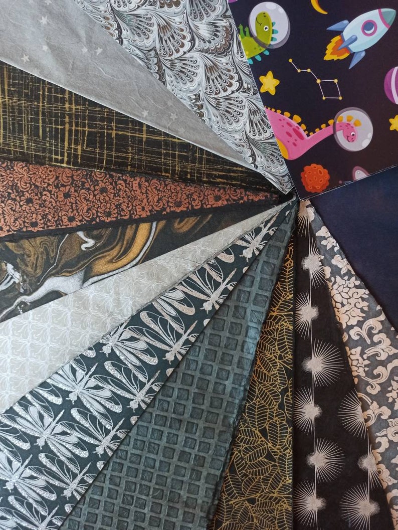 May include: A collection of 15 different patterned tissue papers in various colors, including black, white, gold, and silver. The papers are arranged in a fan shape, with the patterns visible on each sheet.