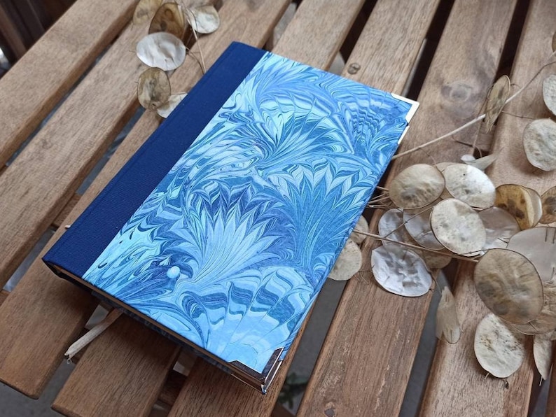 May include: A blue and white marbled notebook with a dark blue spine. The notebook is lying on a wooden surface.