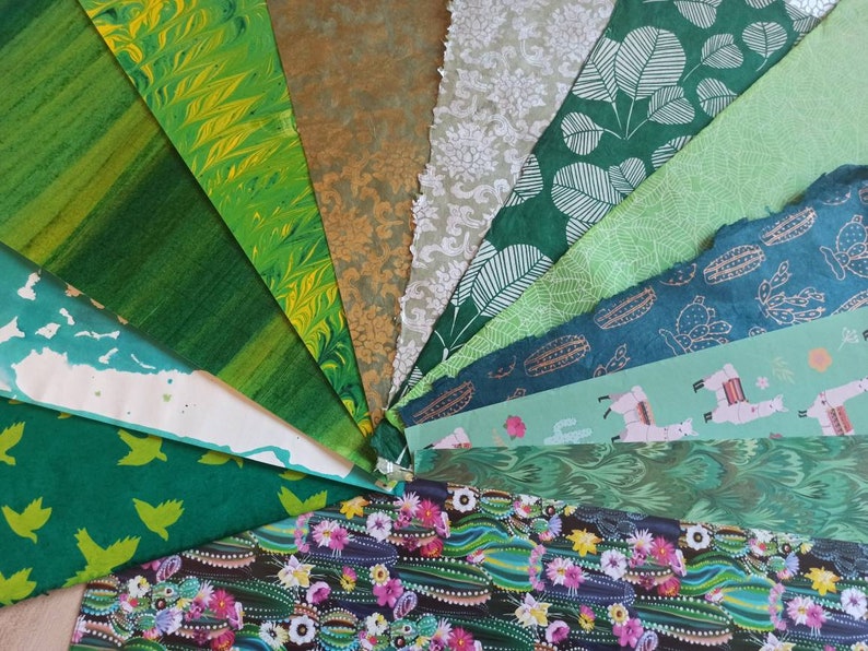 May include: A collection of green patterned papers with various designs, including marbled, floral, and geometric patterns. The papers are arranged in a fan shape, showcasing the different textures and colors.