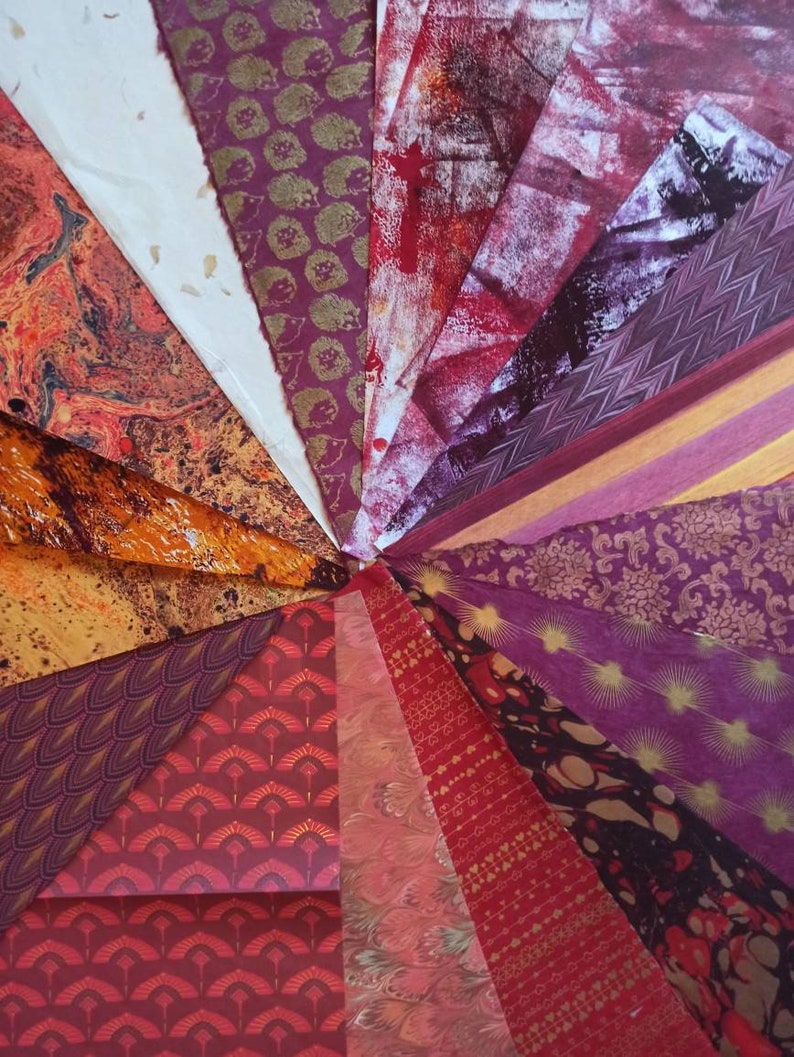 May include: A collection of patterned papers in shades of red, orange, and purple. The papers are arranged in a radial pattern, with the center of the pattern being at the top of the image. The papers have a variety of patterns, including marbled, geometric, and floral.