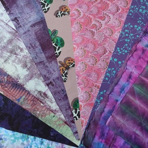 May include: A collection of patterned papers in shades of purple, pink, and blue. The papers feature various designs, including butterflies, floral patterns, and abstract designs.