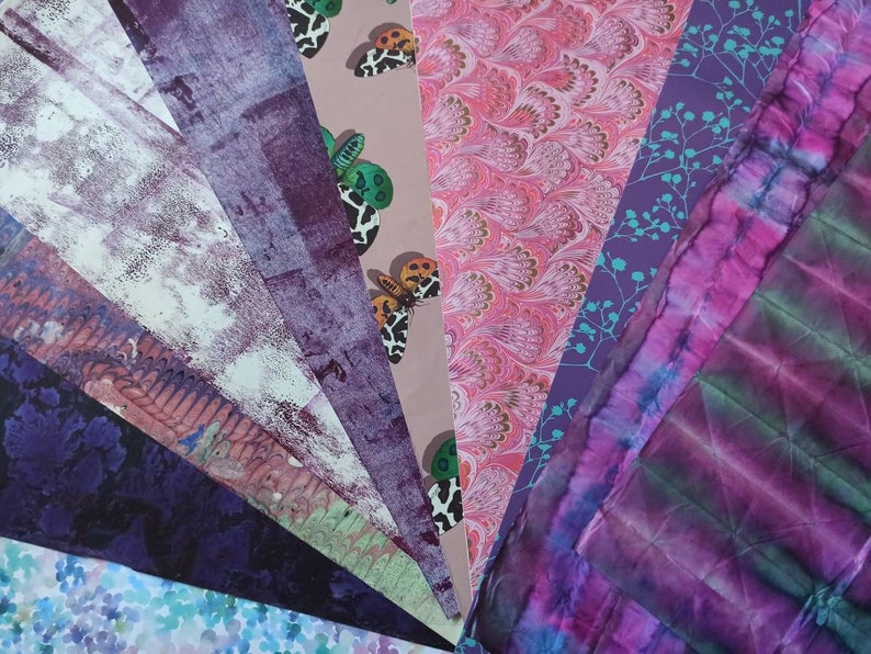 May include: A collection of patterned papers in shades of purple, pink, and blue. The papers feature various designs, including butterflies, floral patterns, and abstract designs.