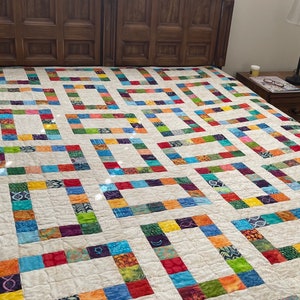 May include: A colorful patchwork quilt with a white background and a geometric pattern. The quilt is made of squares of different colors and patterns, and it is laid out on a bed.