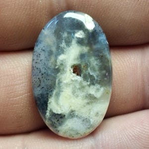 Peut inclure: Pierre précieuse de forme ovale avec une surface polie. La pierre présente un mélange de couleurs, notamment du gris, du blanc et des nuances de marron. Le motif ressemble à un ciel nuageux avec des détails mouchetés.