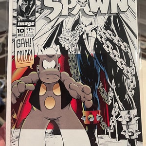 May include: Comic book cover featuring Spawn, a red and black superhero with a skull on his chest, standing in front of a gray and white character with a speech bubble that says "GAH! COLOR!" The comic book is titled "Spawn" and is issue number 10.