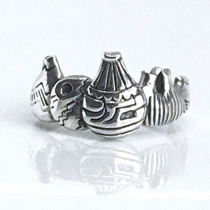May include: A silver ring with a design of four pottery vessels. Each vessel has unique etched patterns and shapes, with a polished finish. The ring is set against a white background, highlighting the intricate details of the jewellery.
