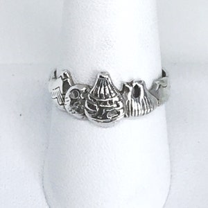 May include: A silver ring featuring a design of several small, detailed, three-dimensional figures. The ring is displayed on a white stand.