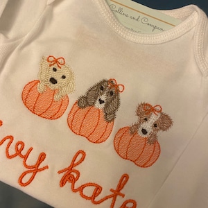Pode incluir: Macac&atilde;o branco com ab&oacute;boras e c&atilde;es bordados. O texto "baby kate" est&aacute; bordado no macac&atilde;o.