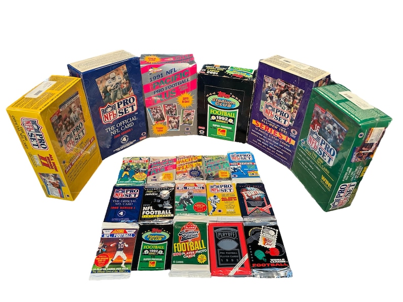 May include: A collection of unopened packs of 1991 and 1992 NFL Pro Set trading cards. The packs are arranged in a semi-circle with the newer packs in the front. The packs are all in various colors, including red, blue, green, and yellow. The packs feature the NFL Pro Set logo and the year of the cards.