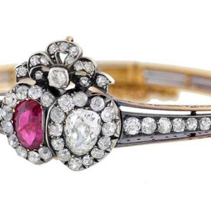 Puede incluir: Un brazalete de oro y plata con un diseño de corazón de rubí y diamantes. El corazón está rodeado de diamantes más pequeños y el brazalete tiene un delicado diseño floral.