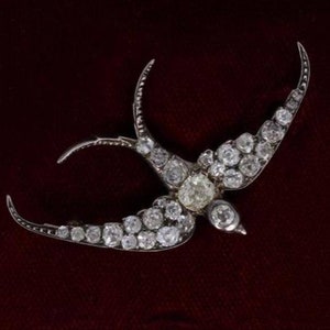 Pode incluir: Um broche de andorinha de prata e diamantes. A andorinha é adornada com pequenos diamantes e tem um diamante maior no centro do peito.
