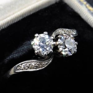 May include: A silver ring with two round diamonds set in a twisted band. The diamonds are surrounded by smaller diamonds.
