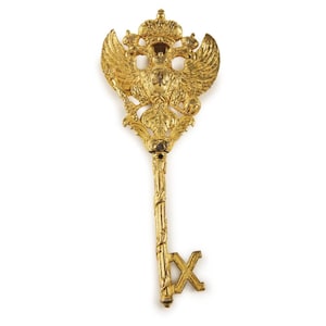 May include: A gold-colored key with a double-headed eagle design. The eagle is holding a shield with the letter "C" on it. The key has a cross-shaped handle.