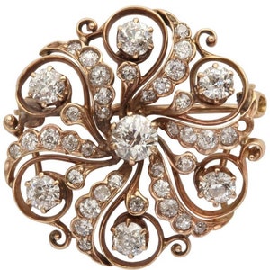 May include: A vintage diamond brooch with a swirling floral design set in 14k gold. The brooch features a large central diamond surrounded by smaller diamonds.