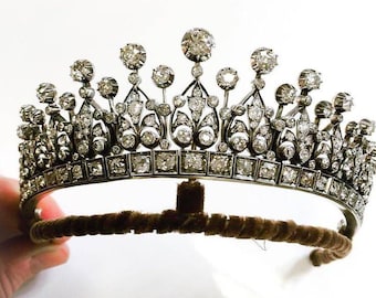 May include: A silver tiara with a row of square-shaped diamonds and a row of round diamonds above it. The tiara has a delicate floral design and is adorned with many diamonds.