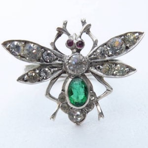 May include: A silver bee brooch featuring a green gemstone and clear rhinestones. The bee's wings are outstretched and the body is adorned with intricate silver detailing.
