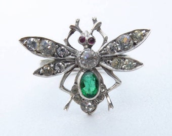 May include: A silver bee brooch with a green gemstone and clear rhinestones. The bee's wings are spread out and the body is detailed with intricate silverwork.