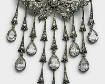 May include: A silver and diamond brooch with a circular design featuring a bow and dangling teardrop-shaped diamonds.