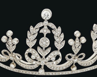 Könnte beinhalten: Eine silberne Tiara mit einem filigranen Design, das einen zentralen Bogen und Blätter zeigt, verziert mit funkelnden Diamanten.