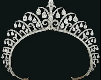 May include: A silver tiara with a symmetrical design, featuring numerous clear, sparkling gemstones. The tiara has a curved base and a series of arching elements, each adorned with teardrop-shaped gems. A large, central gem tops the design.