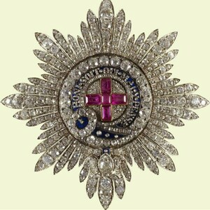 May include: A large, diamond-encrusted star-shaped brooch with a central circular medallion. The medallion features a red cross with a blue enamel background and the inscription "HONI SOIT QUI MAL Y PENSE".