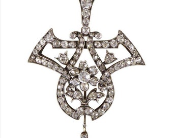 May include: A silver pendant with a delicate, intricate design set with sparkling diamonds. The pendant features a floral motif with a teardrop-shaped diamond hanging from the bottom.