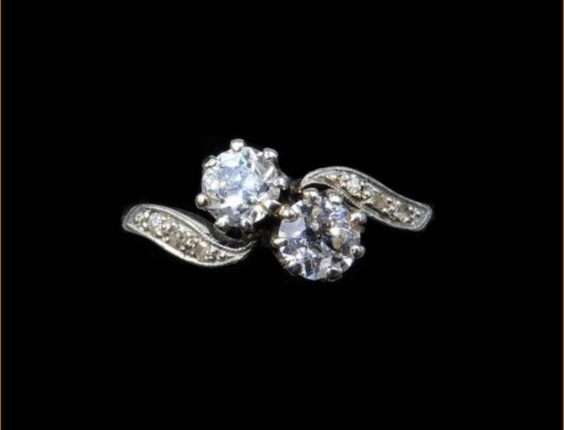 May include: A silver ring with two round diamonds set in a swirling design.