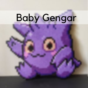 Op de afbeelding: Een paars en wit gepixeld pluche speelgoed van een Gengar Pokémon-personage. Het speelgoed zit op een donkergrijs oppervlak. De tekst "Baby Gengar" staat boven het speelgoed.