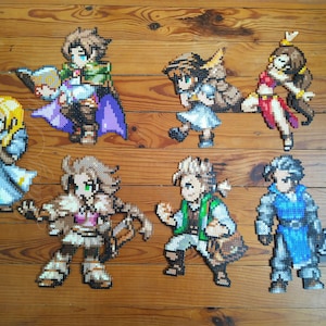 Puede incluir: Un conjunto de ocho figuras de pixel art, cada una representando un personaje diferente. Las figuras est&aacute;n hechas de cuentas de colores y est&aacute;n dispuestas sobre una superficie de madera. Los personajes incluyen una guerrera con una espada, un mago con un bast&oacute;n, una arquera con un arco y flechas, un caballero con un escudo, una sanadora con un bast&oacute;n, un ladr&oacute;n con una daga, una bardo con un la&uacute;d y un monje con un bast&oacute;n.