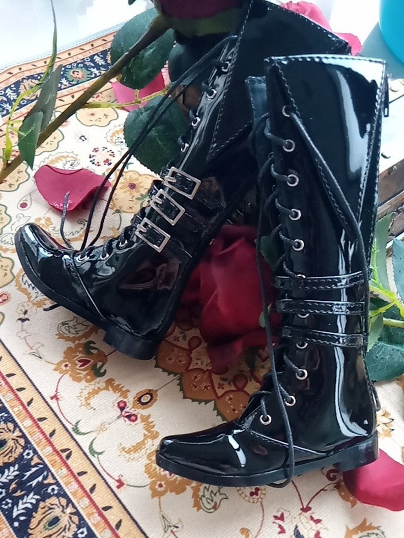 May include: A pair of black patent leather knee-high boots with buckles and laces. The boots have a pointed toe and a low heel.