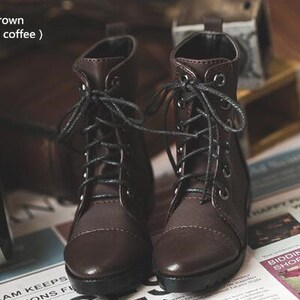 May include: A pair of brown leather lace-up boots with black laces. The boots have a slightly distressed look and are sitting on a newspaper.