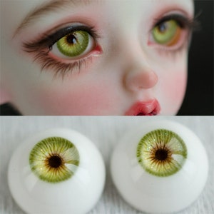 May include: A pair of green glass eyes with brown irises and gold flecks. The eyes are designed for dolls and have a realistic appearance.