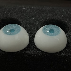K&ouml;nnte beinhalten: Zwei wei&szlig;e Puppenaugen mit blauer Iris und hellblauer Pupille.