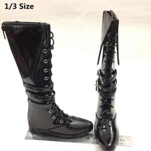 May include: A pair of black patent leather knee-high boots with lace-up fronts and buckle accents. The boots have a pointed toe and a low heel. The boots are 1/3 size.