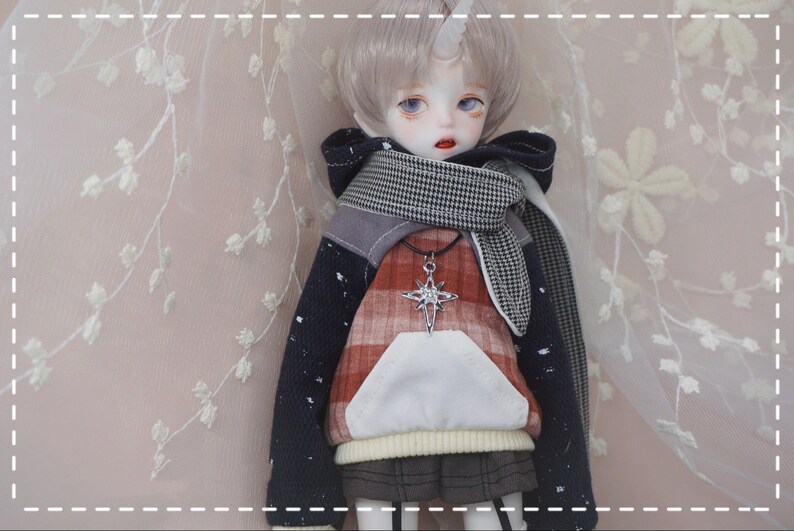 May include: A doll with short, silver hair wearing a red and black plaid hoodie with a white pocket, a black and white checkered scarf, and a silver star pendant necklace.