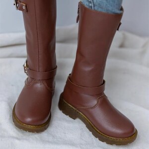 May include: A pair of brown leather knee-high boots with buckles and zippers. The boots have a chunky heel and a rounded toe.