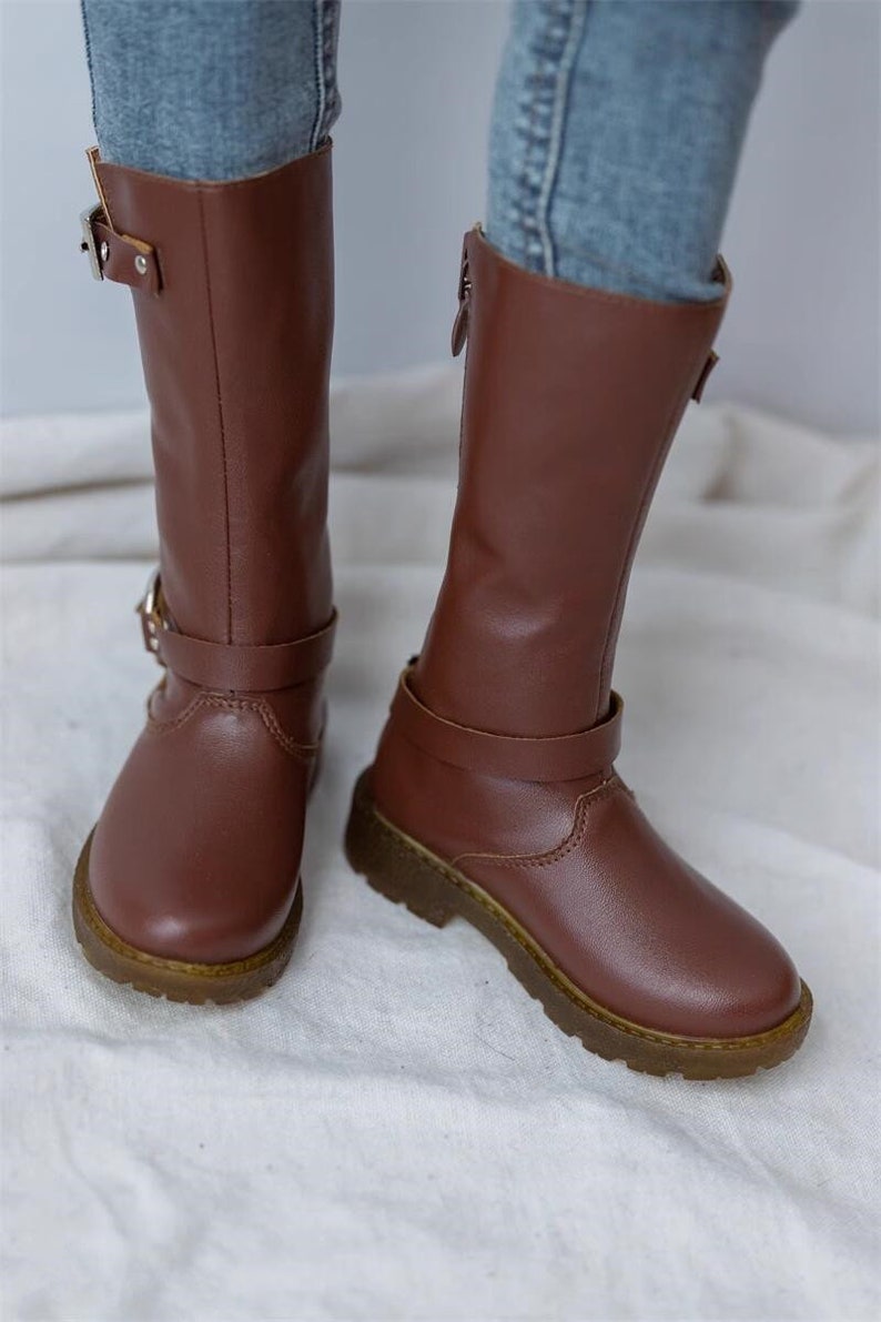 May include: A pair of brown leather knee-high boots with buckles and zippers. The boots have a chunky heel and a rounded toe.