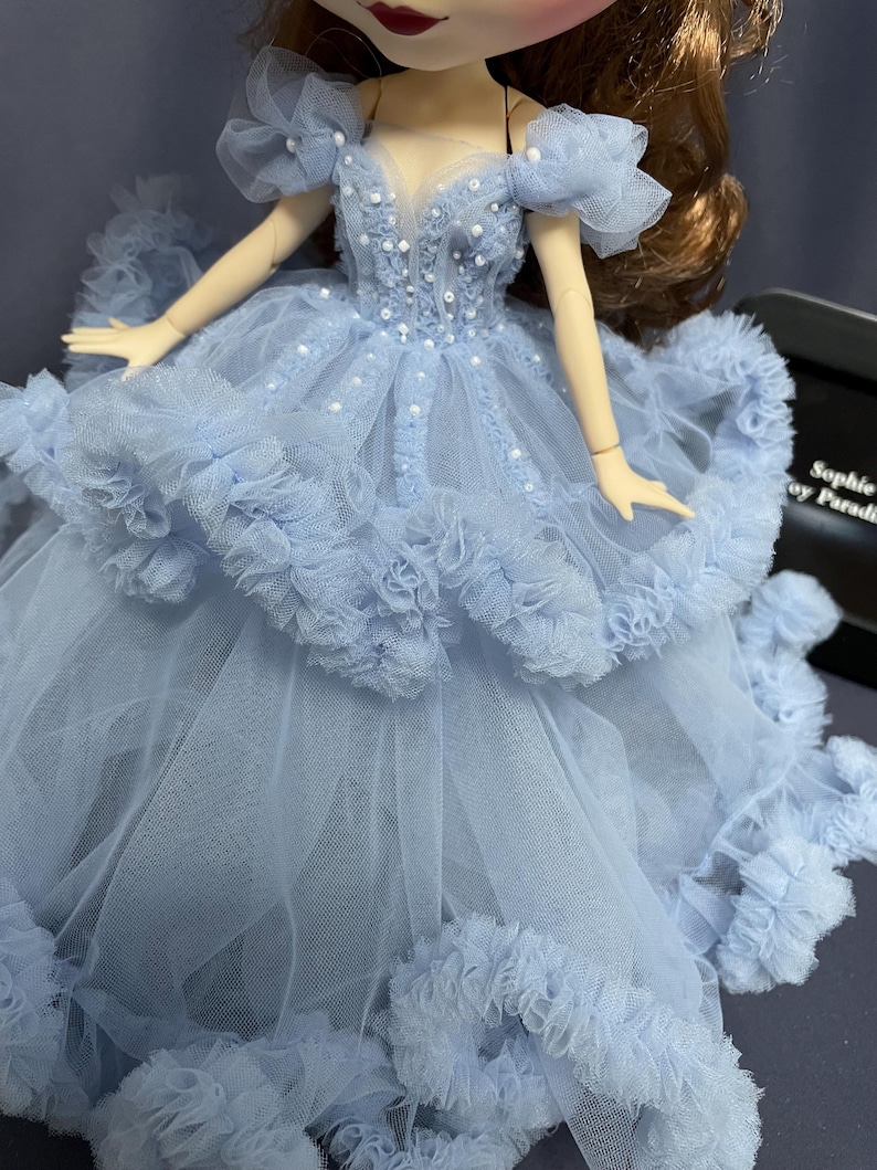 May include: A light blue tulle dress with a sweetheart neckline and ruffled trim. The dress is decorated with white beads and has a layered skirt.